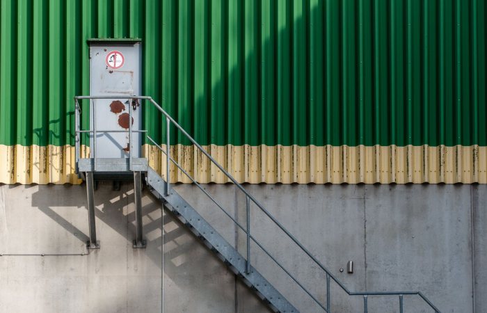Metal staircase against a corrugated metal wall, capturing industrial architecture with shadows on a sunny day.