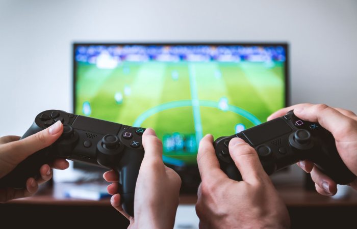 Close-up of hands holding gaming controllers in front of a TV. Engaged in a video gaming session.