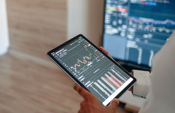 A person uses a tablet to monitor stock market trends and real-time trading graphs.