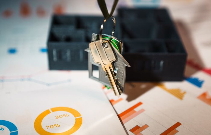 Real estate keys on house keychain with financial graphs, symbolizing property investment.