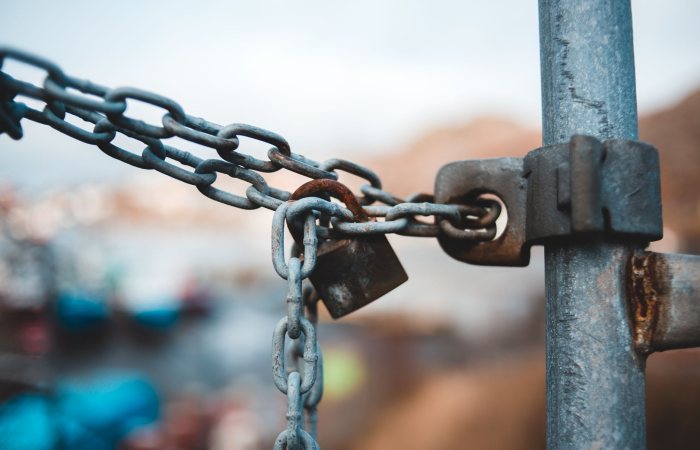 Old metal chain with rustic lock hanging on fence on street against blurred background in daytime
