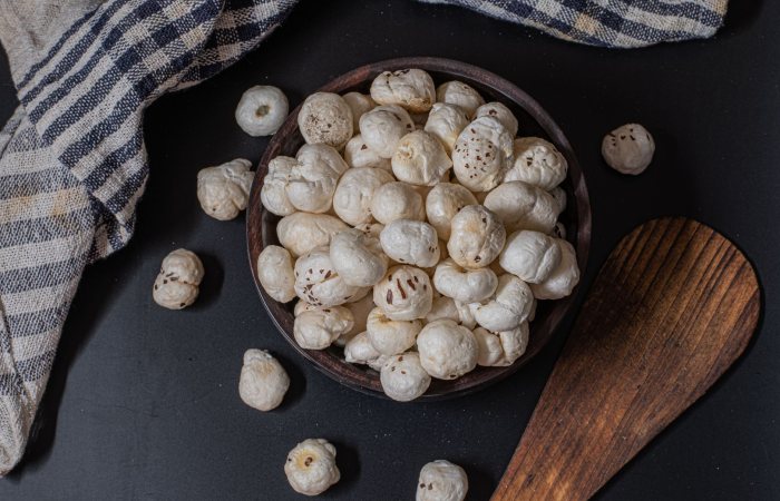 A rustic bowl filled with puffed lotus seeds on a black background, perfect for snacks.