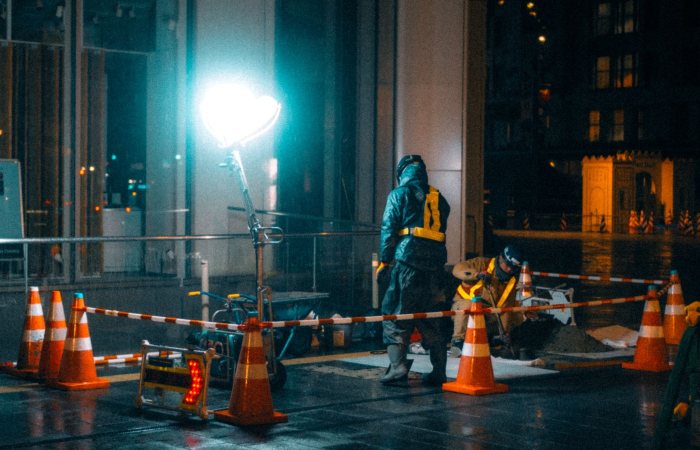 Construction workers at night in a city with bright lights and reflections.