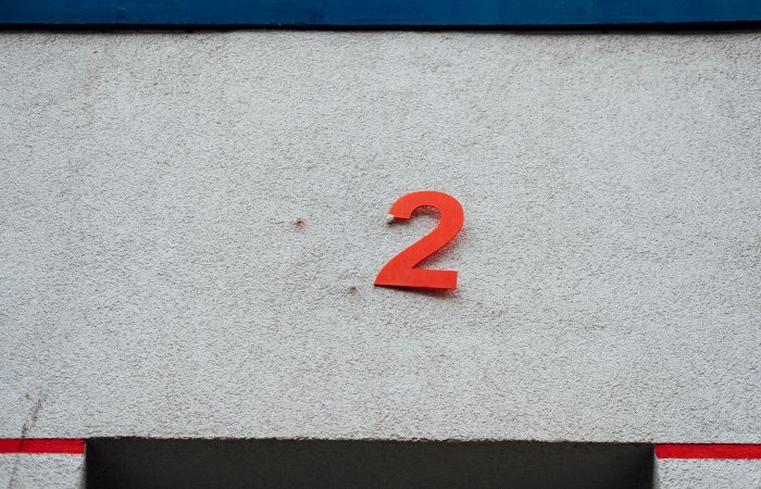 A simple red number 2 on a textured concrete wall with minimalistic design elements.