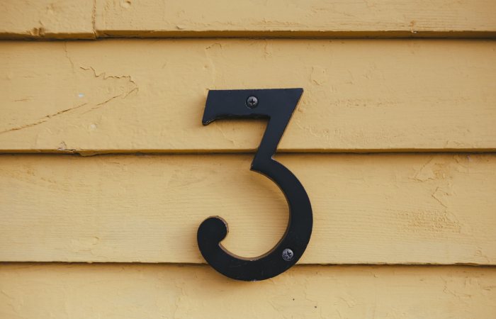 Close-up of a black number three sign mounted on a textured yellow wooden wall.