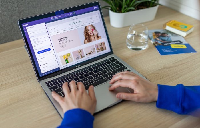 Hands typing on a laptop showing an e-commerce website in a modern office setting.