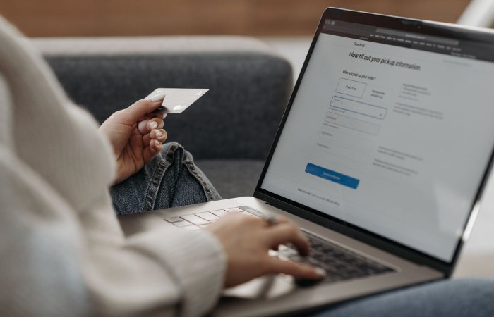 Woman holding credit card shopping online on a laptop from a couch.