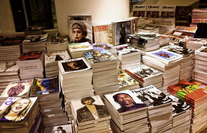 Huge stacks of diverse fashion and lifestyle magazines piled high in an indoor store setting.