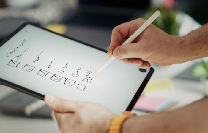 Close-up of a hand writing on a digital checklist using a stylus on a tablet, enhancing productivity.