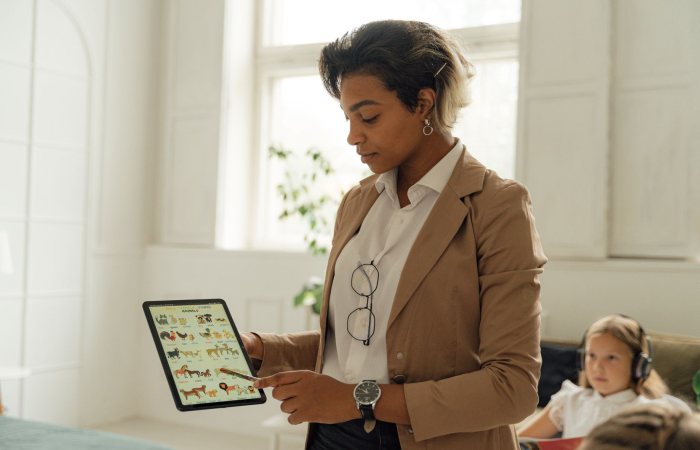 A teacher using a tablet in a bright classroom to explain a lesson to a student.